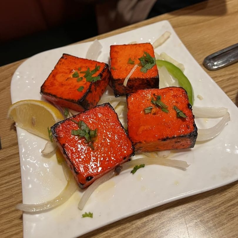 Four pieces of bright orange paneer tikka, garnished with herbs, onions, and a lemon wedge.