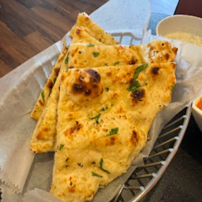 Golden brown naan bread, garnished with herbs, served in a metal basket at Curry Place Germantown.