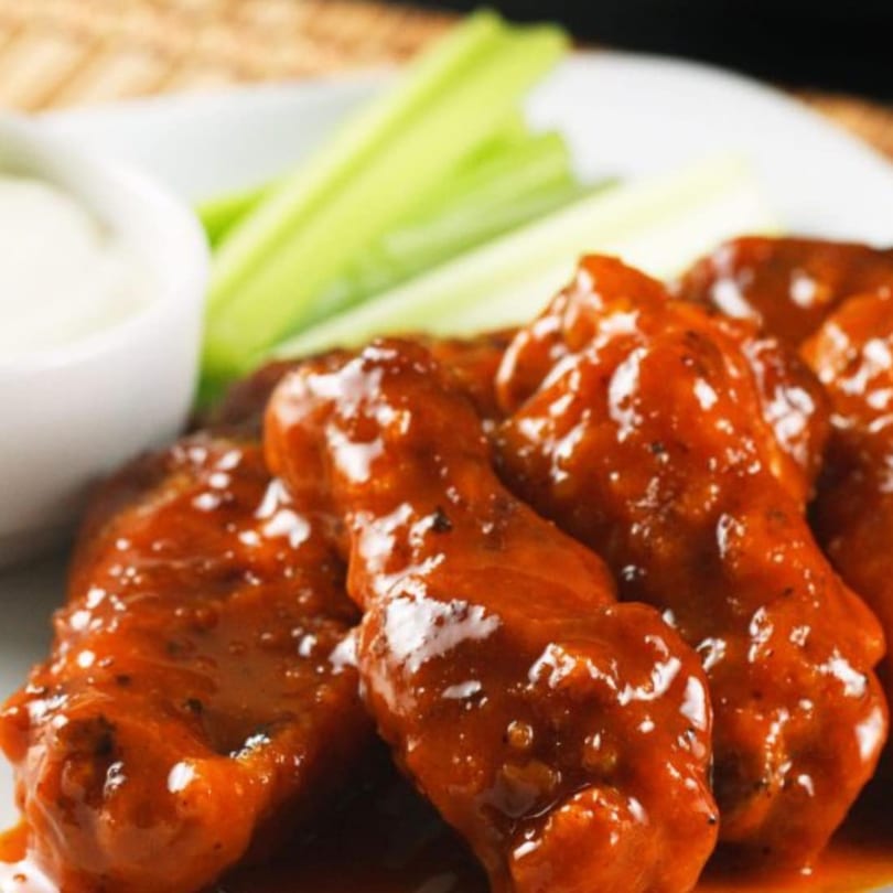 Spicy chicken wings with celery sticks and a side of ranch dressing on a white plate.