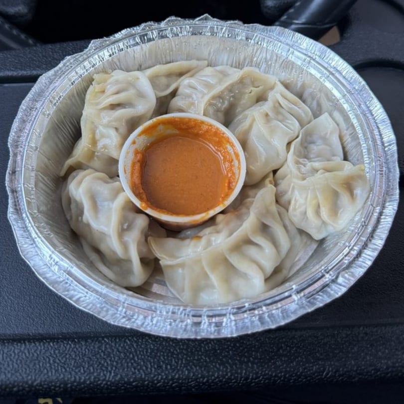 Steamed momos with a side of orange dipping sauce in a foil container from Curry Place Germantown.