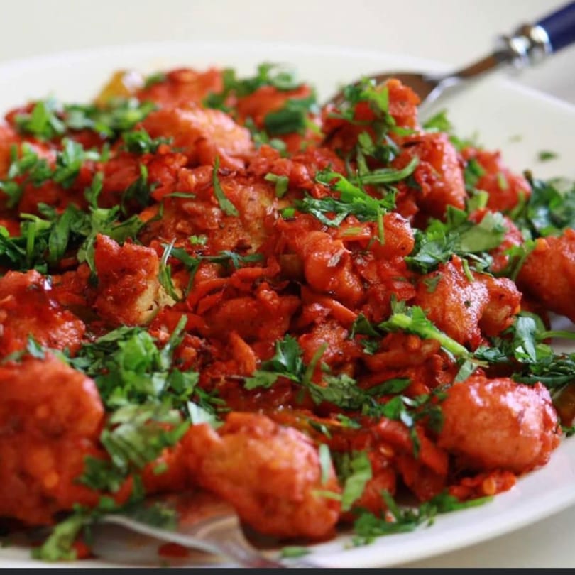 Close-up of Indian chili chicken, vibrant red with green cilantro, on a white plate.